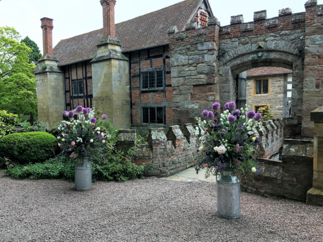 Milk churn displays with Alliums, Roses, and Peonies at Birtsmorton Court. Floral design by Cotswold Blooms, wedding florist based in Cheltenham.