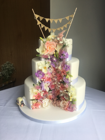Wedding cake sliced and filled with pastel flowers. Floral design by Cotswold Blooms, wedding florist based in Cheltenham.
