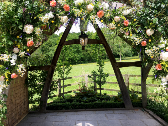 Bright natural arch display with Daisy’s, Craspedia, Miss Piggy Roses and Thlaspi at Hyde House. Floral design by Cotswold Blooms, wedding florist based in Cheltenham.
