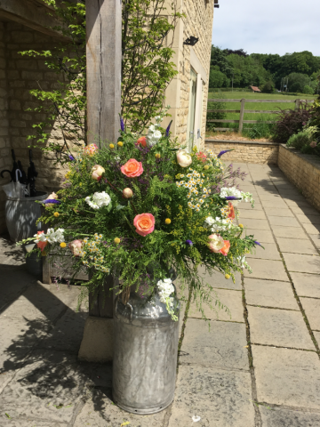 Country garden milk churn of Daisy’s, Craspedia, Miss Piggy Roses and Thlaspi at Hyde House. Floral design by Cotswold Blooms, wedding florist based in Cheltenham.