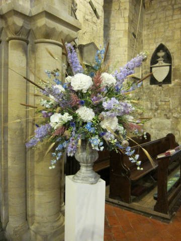 Urn display in white and Lilac including Delphinium, Hydrangea and dried crops for a church wedding. Floral design by Cotswold Blooms, wedding florist based in Cheltenham.