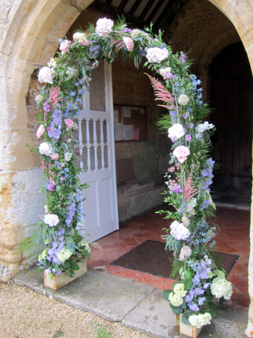 Freestanding arch display at Withington Church including Astilbe, Delphinium and Hydrangea. Floral design by Cotswold Blooms, wedding florist based in Cheltenham.