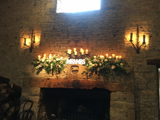 Cripps Barn mantel piece dressed with natural flowing displays with candles. Floral design by Cotswold Blooms, wedding florist based in Cheltenham.