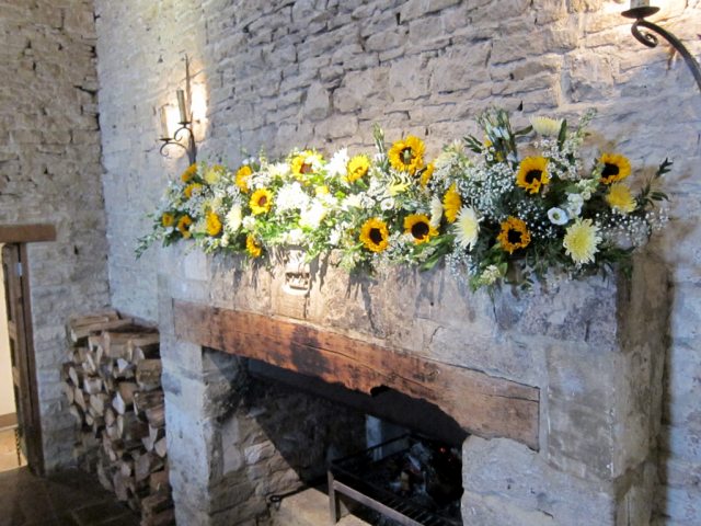 Sunflowers and white Gypsophila, Eustoma and foliage on the mantel piece at Cripps Barn. Floral design by Cotswold Blooms, wedding florist based in Cheltenham.