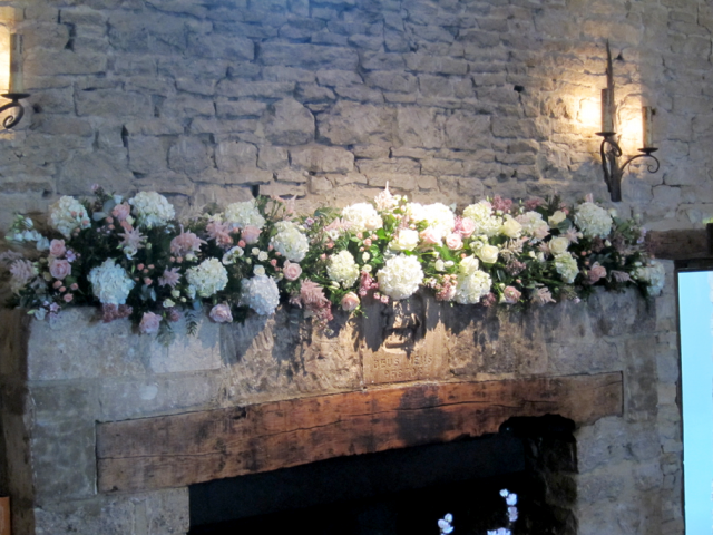 White and light pink mantel piece display of Astilbe, Hydrangea, Roses and spray Roses at Cripps Barn. Floral design by Cotswold Blooms, wedding florist based in Cheltenham.