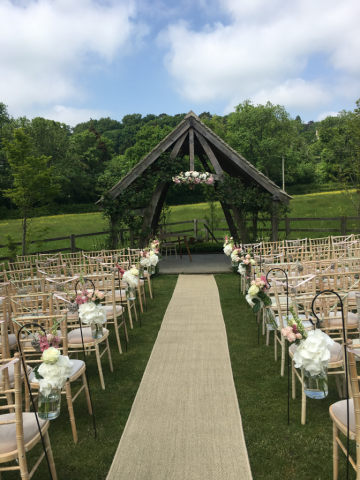 Outdoor ceremony with aisle markers and arbour display at Hyde House. Floral design by Cotswold Blooms, wedding florist based in Cheltenham.