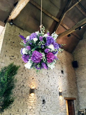 Flower ball hanging in Cripps Barn including Hydrangea, Stocks and Delphinium. Floral design by Cotswold Blooms, wedding florist based in Cheltenham.