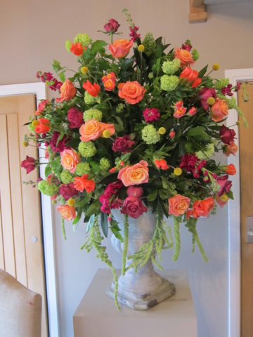 Coral, lime green and raspberry natural urn display including Roses, Stocks and Amaranthus. Floral design by Cotswold Blooms, wedding florist based in Cheltenham.