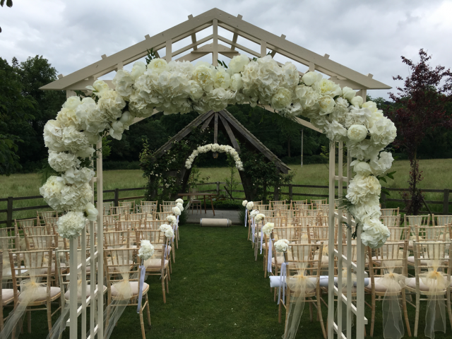 White Hydrangea and Peonie arches dressing an outdoor ceremony at Hyde House. Floral design by Cotswold Blooms, wedding florist based in Cheltenham.