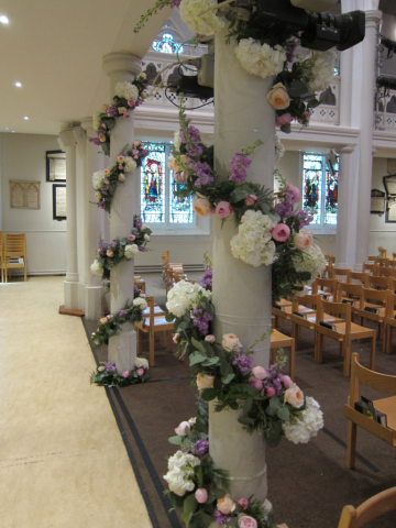 Peach, lilac and white country garden pillar display at Holy Trinity Brompton, London. Floral design by Cotswold Blooms, wedding florist based in Cheltenham.