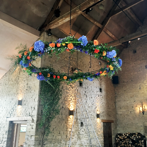 Bright orange and blue flower halo including Gladioli, Dahlia and Roses outside Cripps Barn. Floral design by Cotswold Blooms, wedding florist based in Cheltenham.