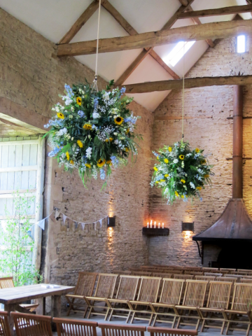 Hanging flowers at Cripps Stone Barn including Sunflowers, Delphinium, and mixed foliage. Floral design by Cotswold Blooms, wedding florist based in Cheltenham.