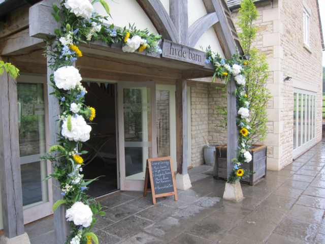 Entrance display of Hydrangea, Sunflowers, light blue Delphinium and mixed foliage. Floral design by Cotswold Blooms, wedding florist based in Cheltenham.