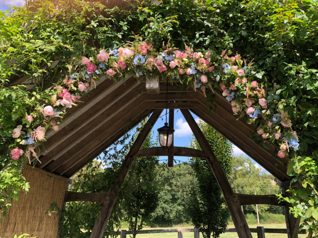 Light blue and pink arch display for an outdoor ceremony at Hyde House. Floral design by Cotswold Blooms, wedding florist based in Cheltenham.