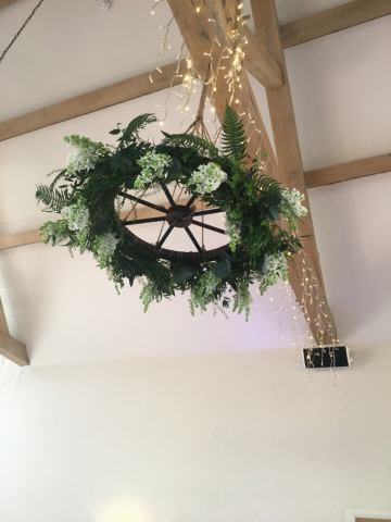 Wagon wheel with white lilac and fern. Floral design by Cotswold Blooms, wedding florist based in Cheltenham.
