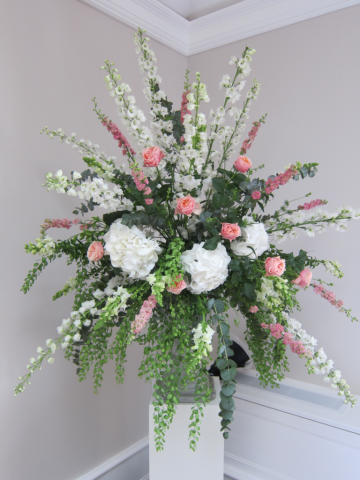 Pedestal display in white and coral with mixed foliage at Foxhill Manor. Floral design by Cotswold Blooms, wedding florist based in Cheltenham.