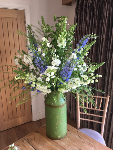 Natural urn display in light blue and white including Delphinium, Stocks, Phlox and Snap Dragons. Floral design by Cotswold Blooms, wedding florist based in Cheltenham.