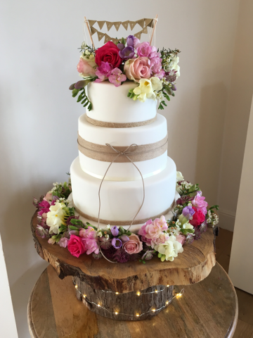 Wedding cake dressed with country garden display on the top and around the base in pastel shades. Floral design by Cotswold Blooms, wedding florist based in Cheltenham.
