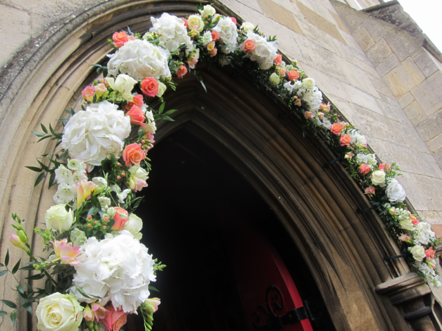 Coral and white Roses, Hydrangea, Hypericum and Freesia at St Mary’s Church, Charlton Kings. Floral design by Cotswold Blooms, wedding florist based in Cheltenham.