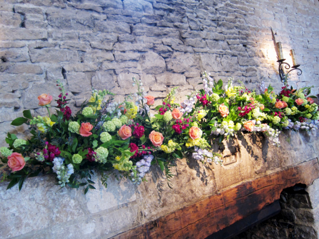 Bright and bold mantel piece display in coral, lime green, yellow and raspberry at Cripps Barn. Floral design by Cotswold Blooms, wedding florist based in Cheltenham.