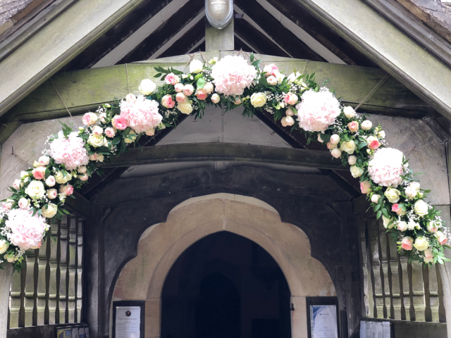 Church entrance in light pink and white including Hydrangea, Roses and Gypsophila. Floral design by Cotswold Blooms, wedding florist based in Cheltenham.