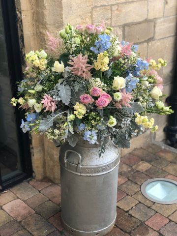 Milk churn display in light pink, blue and white outside the ceremony at Ellenborough Park. Floral design by Cotswold Blooms, wedding florist based in Cheltenham.