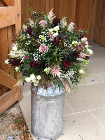 Milk churn display in burgundy, light pink and white including Spray Roses, Astilbe, Waxflower and Safari. Floral design by Cotswold Blooms, wedding florist based in Cheltenham.