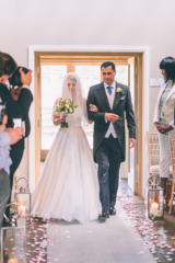 Bride walking down the aisle at Hyde Barn, Stow-on-the-Wold.Floral design by Cotswold Blooms, wedding florist based in Cheltenham.