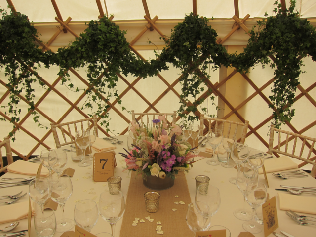 Country garden flower display in a rustic tin, with a backdrop of ivy garlands to dress a wedding yurt. Floral design by Cotswold Blooms, wedding florist based in Cheltenham.