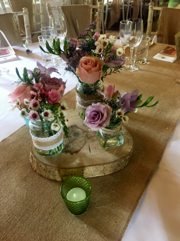 Roses, Wax Flower and Freesia jars on a wood slice at the Green Dragon Inn, Cowley. Floral design by Cotswold Blooms, wedding florist based in Cheltenham.