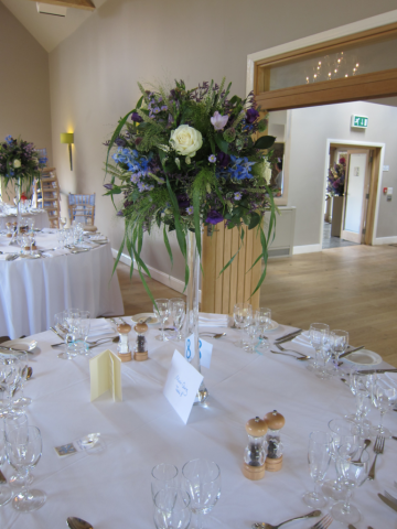 Lily vase table centre, containing white Roses, blue Delphinium and purple Eustoma with Fountain Grass at Hyde House, Stow-on-the-Wold. Floral design by Cotswold Blooms, wedding florist based in Cheltenham.