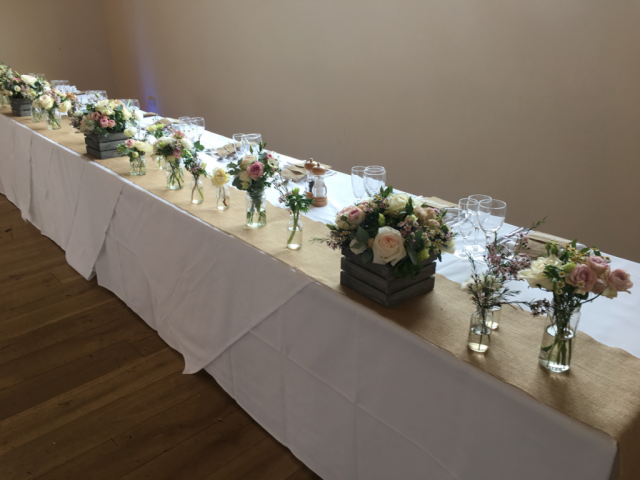 Top table setup, with crates and bottles on a Hessian runner in a country garden style. Floral design by Cotswold Blooms, wedding florist based in Cheltenham.