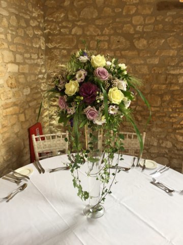 Lily vase display with trailing foliage including Roses, Eustoma Brassica and Wax Flower. Floral design by Cotswold Blooms, wedding florist based in Cheltenham.