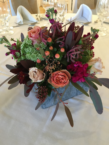 Unique table centre in a slate container, with Rust and Raspberry tones. Floral design by Cotswold Blooms, wedding florist based in Cheltenham.