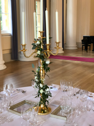 Gold candelabra with white flowers and foliage trailing down, at Pittville Pump Rooms, Cheltenham. Floral design by Cotswold Blooms, wedding florist based in Cheltenham.
