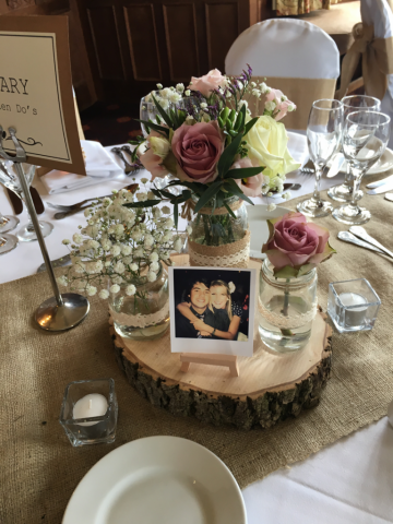 Wood slice and glass jar table display, filled with Gypsophila, Roses and Freesia and Dumbleton Hall. Floral design by Cotswold Blooms, wedding florist based in Cheltenham.