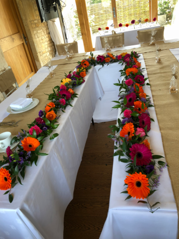 A vibrant Gerbra table display at The Barn at Upcote. Floral design by Cotswold Blooms, wedding florist based in Cheltenham.