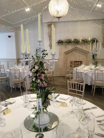 White candelabra and mantel piece displays in lilac and white at Manor by the Lake. Floral design by Cotswold Blooms, wedding florist based in Cheltenham.