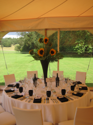 Sunflowers and tropical foliage displays in black lily vases at Bibury Court. Floral design by Cotswold Blooms, wedding florist based in Cheltenham.