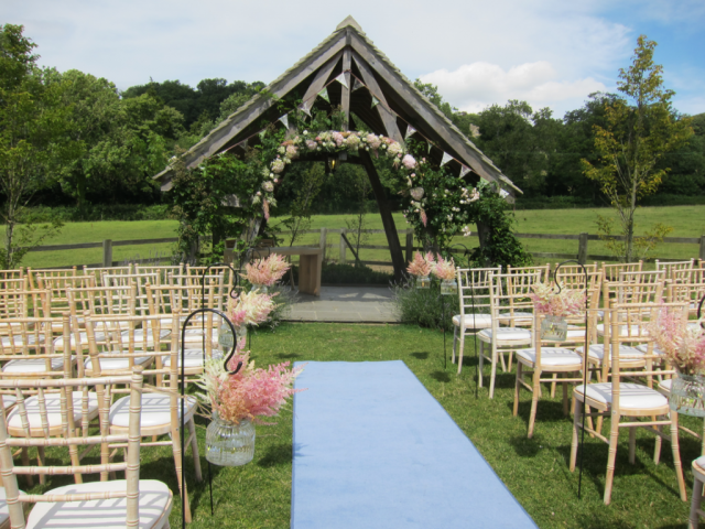 Astilbe isle markers and floral arch creating a stunning outdoor ceremony in the Cotswolds. Floral design by Cotswold Blooms, wedding florist based in Cheltenham.