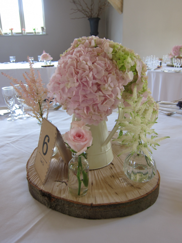 Jug of Hydrangea in soft pink and white on a log slice with specimen vases. Floral design by Cotswold Blooms, wedding florist based in Cheltenham.
