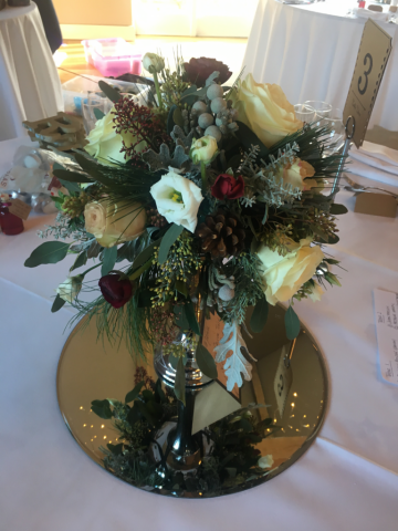 Winter wedding display in red and whites with pine cones, silver foliage’s and roses. Floral design by Cotswold Blooms, wedding florist based in Cheltenham.