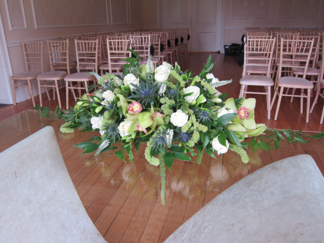 Long and low display with lime greens and blue including Orchids, Amaranthus and Thistle at Eastington Park. Floral design by Cotswold Blooms, wedding florist based in Cheltenham.