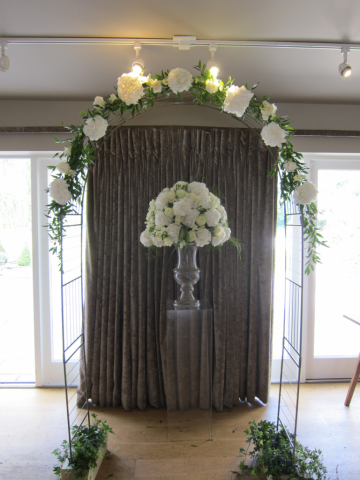 Indoor arch dressed with white Hydrangea and Peonies, with matching pedestal display. Floral design by Cotswold Blooms, wedding florist based in Cheltenham.