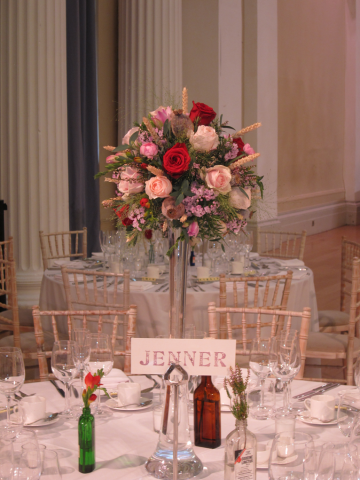 Textured lilly vase ball displays in light pink and red with poppy seeds, wheat, fountain grass, Freesia, Roses and Heather at Pittville pump rooms. Floral design by Cotswold Blooms, wedding florist based in Cheltenham.