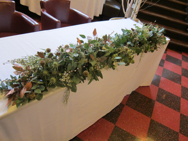 Mixed foliage with Thistle, Genista, and a few coper tones at The Daffodil Cheltenham. Floral design by Cotswold Blooms, wedding florist based in Cheltenham.