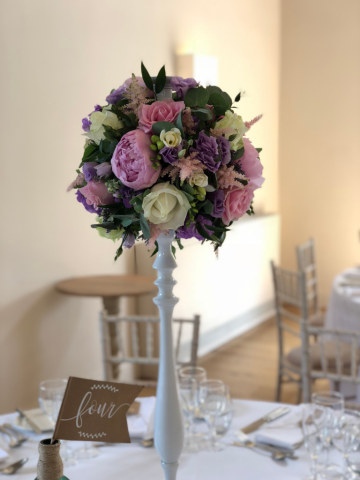 Lilac, light pink and white Peonies, Roses, Eustoma, and Astilbe on a white stand. Floral design by Cotswold Blooms, wedding florist based in Cheltenham.