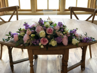 Long and low displays in lilac, light pink and white Peonies, Roses, Eustoma and Astilbe. Floral design by Cotswold Blooms, wedding florist based in Cheltenham.