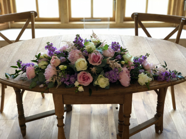 Long and low displays in lilac, light pink and white Peonies, Roses, Eustoma and Astilbe. Floral design by Cotswold Blooms, wedding florist based in Cheltenham.