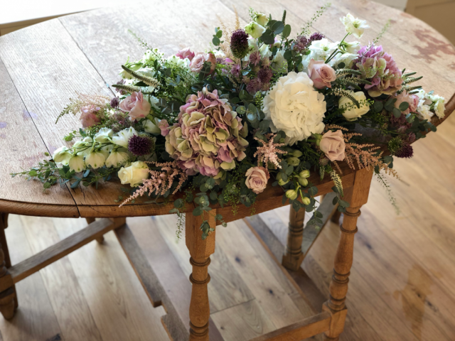 Long and low display in dusky pink shades with touches of burgundy including Hydrangea, Allium, Roses and Eucalyptus. Floral design by Cotswold Blooms, wedding florist based in Cheltenham.